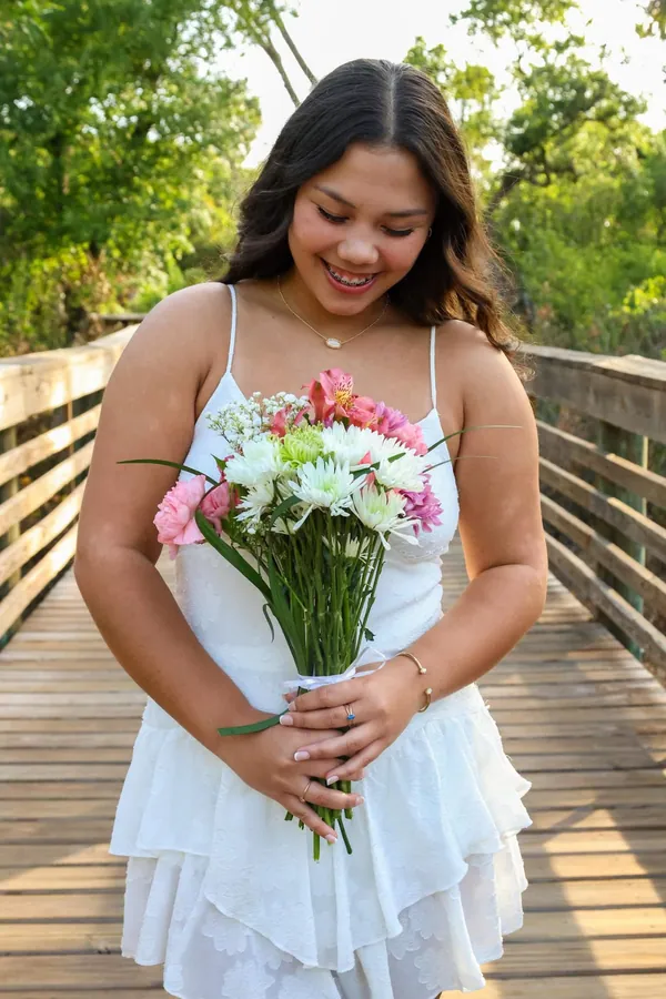 Smiling woman in a white dress standing on a wooden boardwalk with a lush green forest behind her