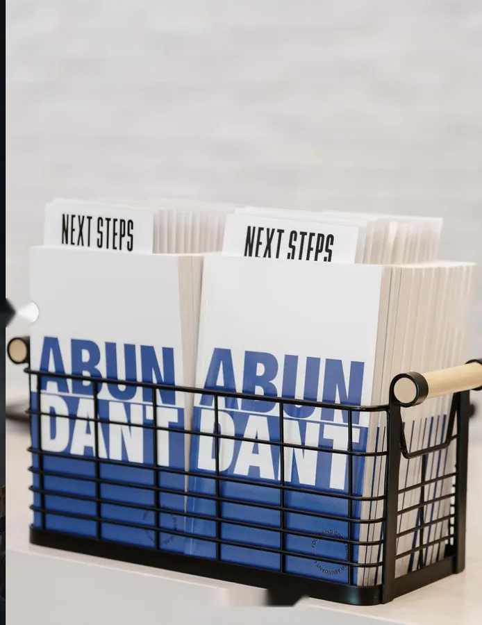 Wire basket holding stacks of Next Steps booklets printed with the word Abundant