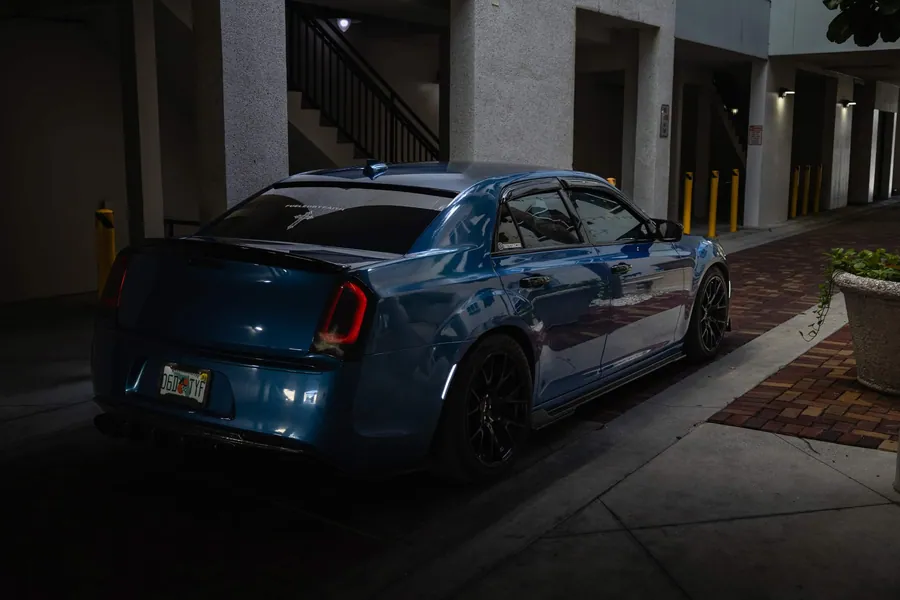 Rear three-quarter view of a deep teal Chrysler 300 at night with illuminated taillights