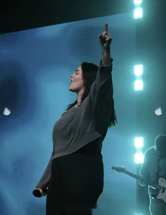 Profile of a woman singing on stage with bright stage lights behind her
