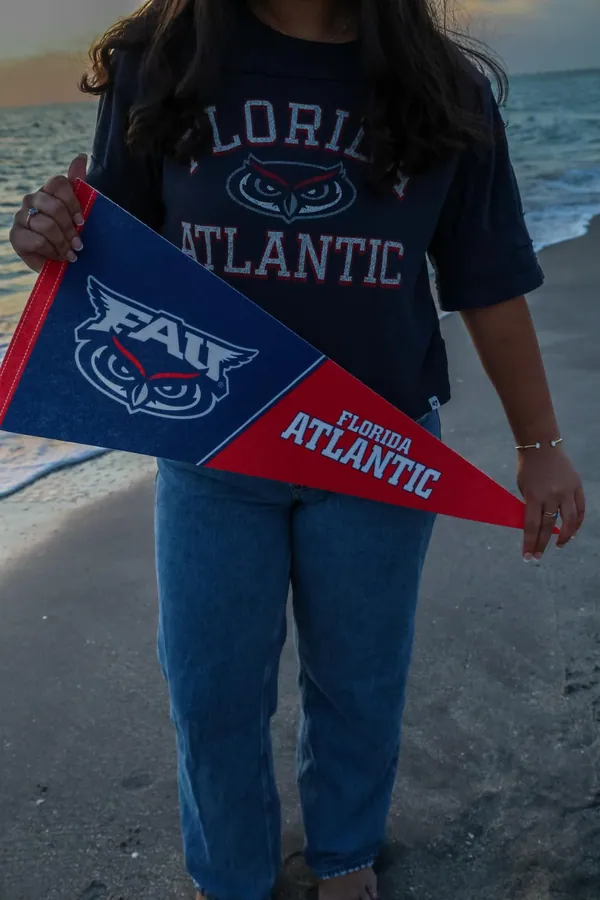 Close detail of a navy and red Florida Atlantic pennant held over a white top on the sand