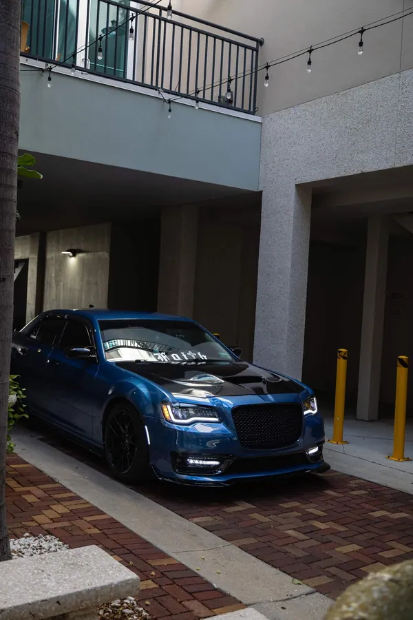 Front-quarter view of a deep teal Chrysler 300 parked in a narrow courtyard between buildings
