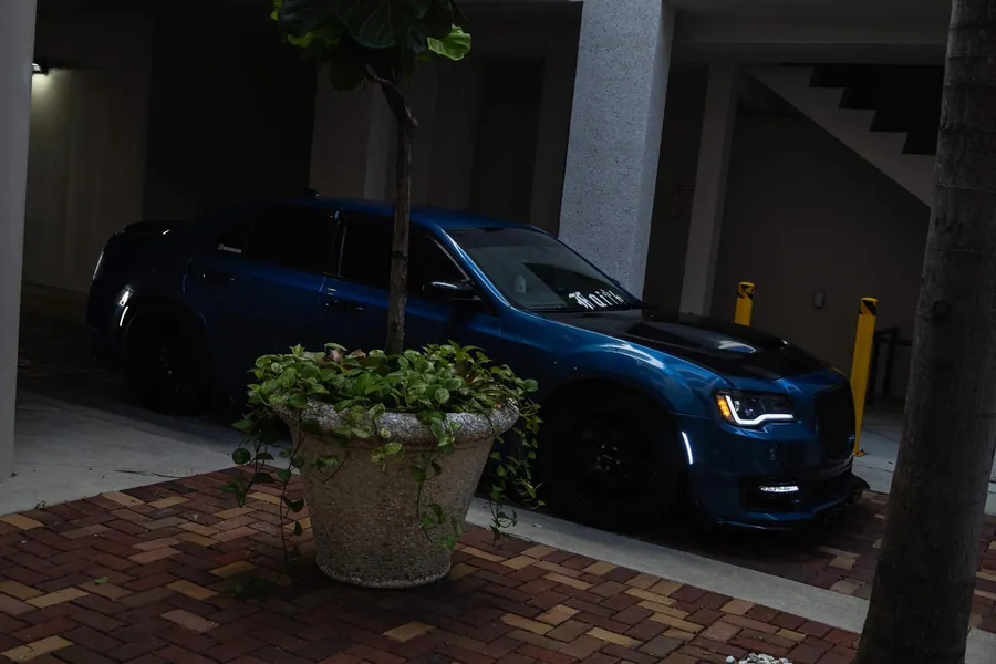 Front view of a deep teal Chrysler 300 parked in a shadowed brick courtyard at night