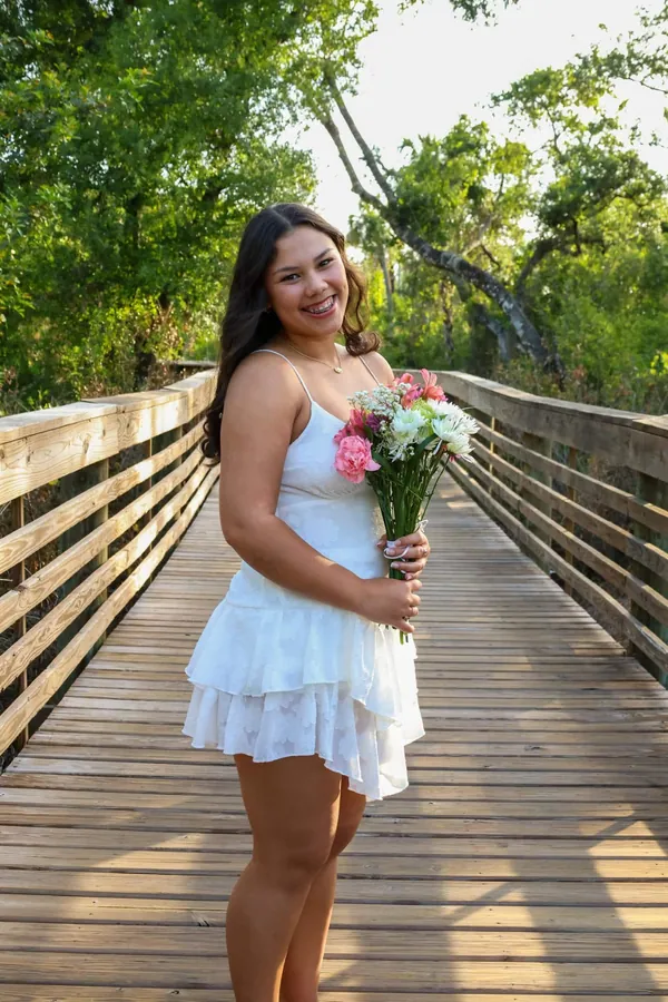 Full-length portrait of a smiling woman in a white dress posing on a wooden boardwalk at sunset