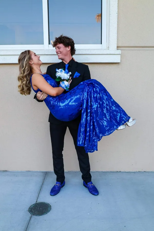 Young man in a black suit lifting his date in a royal blue formal dress, both laughing