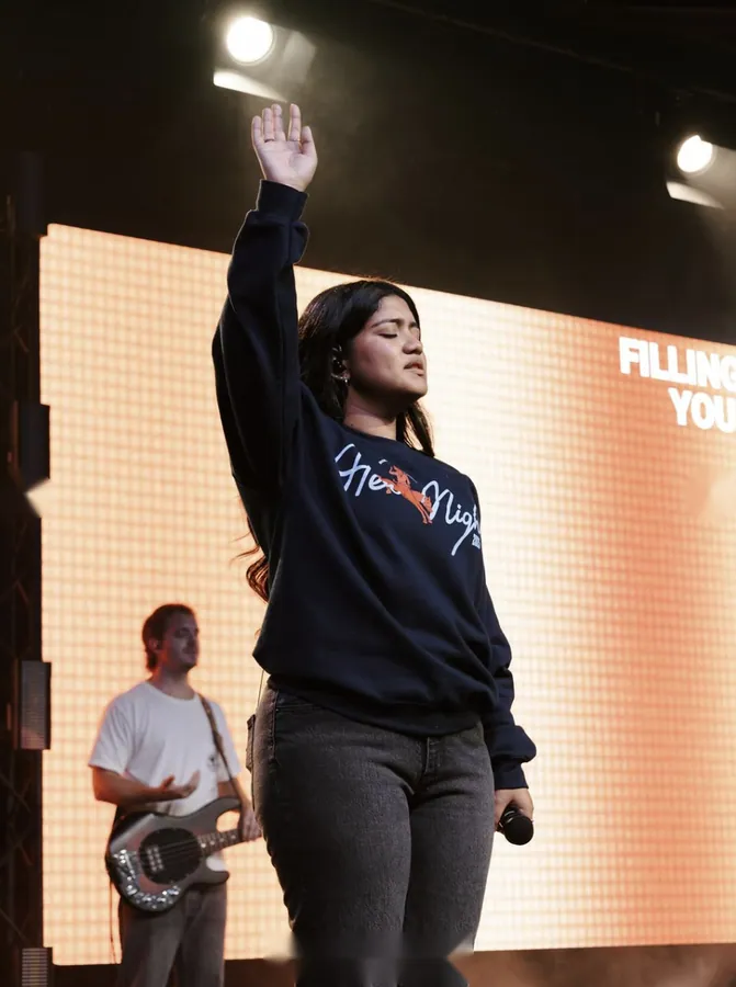 Woman in a sweatshirt with eyes closed and one hand raised in worship