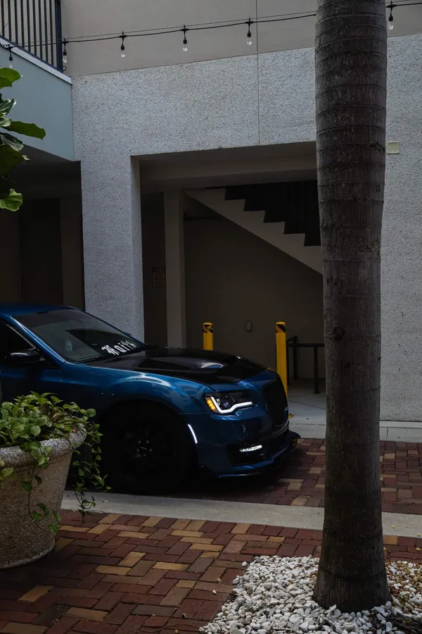 Front end of a deep teal Chrysler 300 parked beneath courtyard string lights