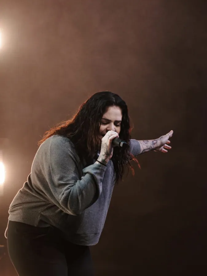 Woman singing with her eyes closed and an arm outstretched on a dark stage