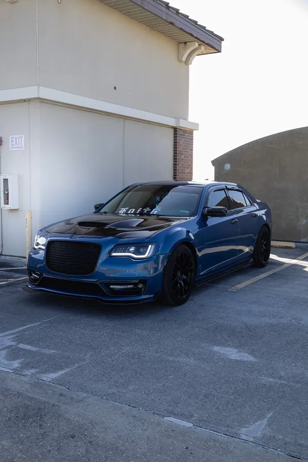 Deep teal Chrysler 300 with a black hood and a Faith window decal parked in daylight