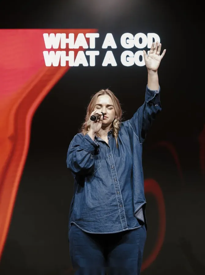Worship leader in a denim shirt singing on stage with one hand raised