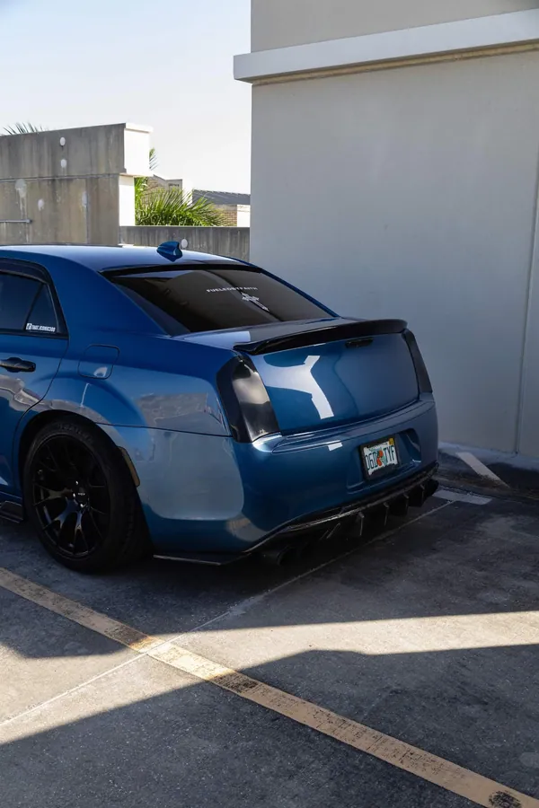Rear view of a deep teal sedan showing the trunk and spoiler in an open lot